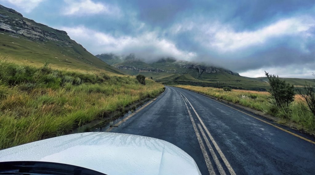 A tarred road curving into the sandstone cliffs of Golden Gate under a dramatic sky, seen from behind the wheel