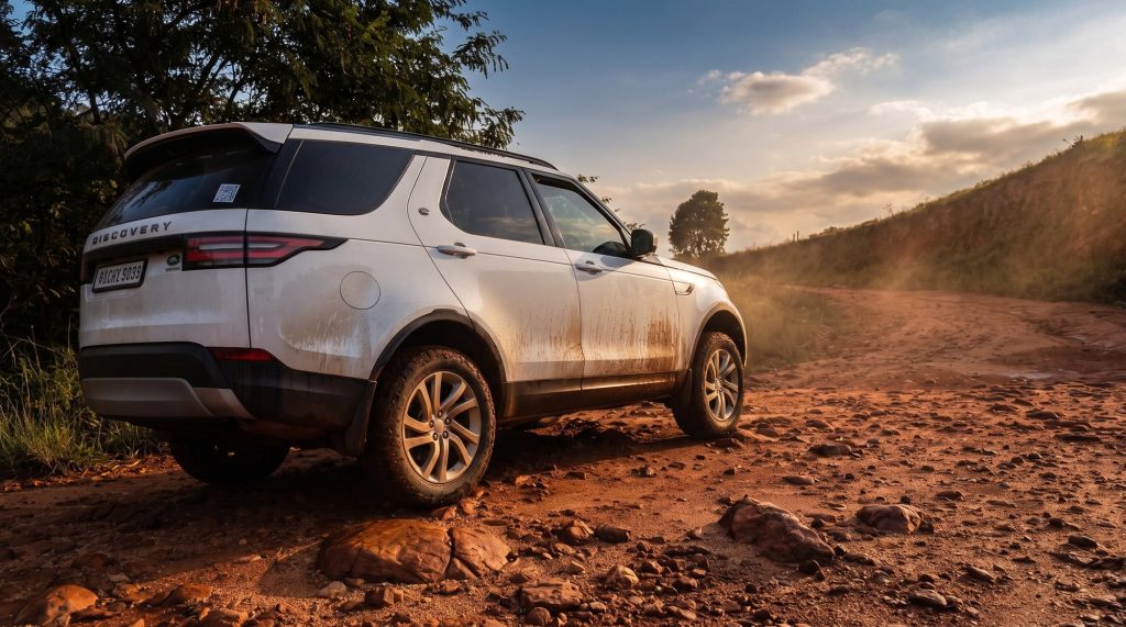 A luxury 4x4 crossing deep red earth on a farm track, dust hanging in the air