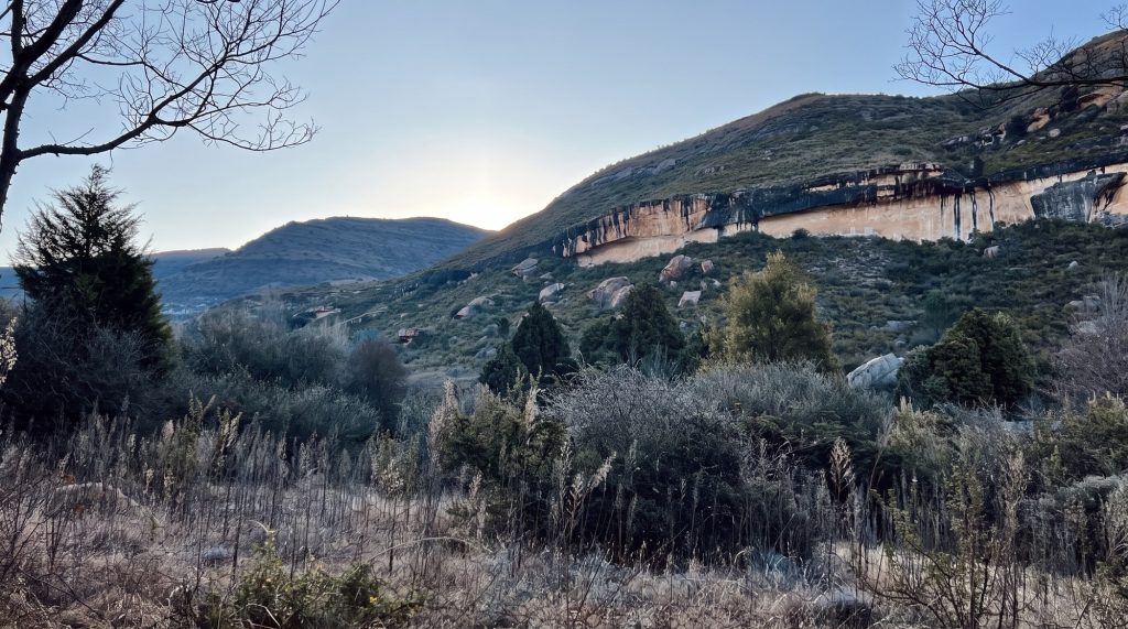 A band of orange sandstone cliff across a hillside above Clarens in low winter light