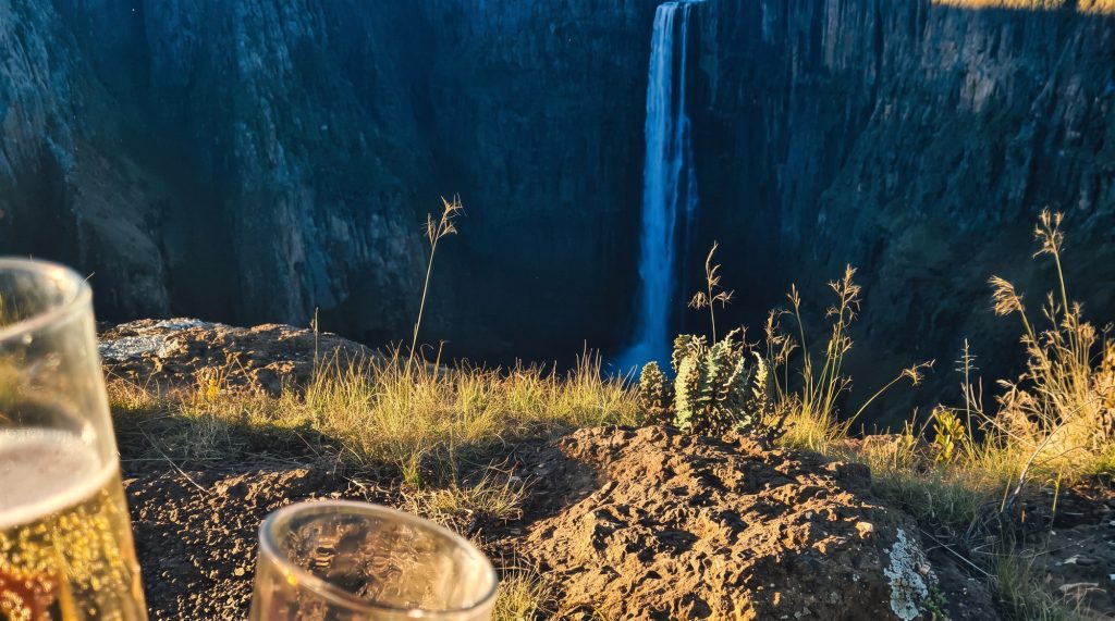 Two glasses raised on the edge of the gorge with Maletsunyane Falls behind
