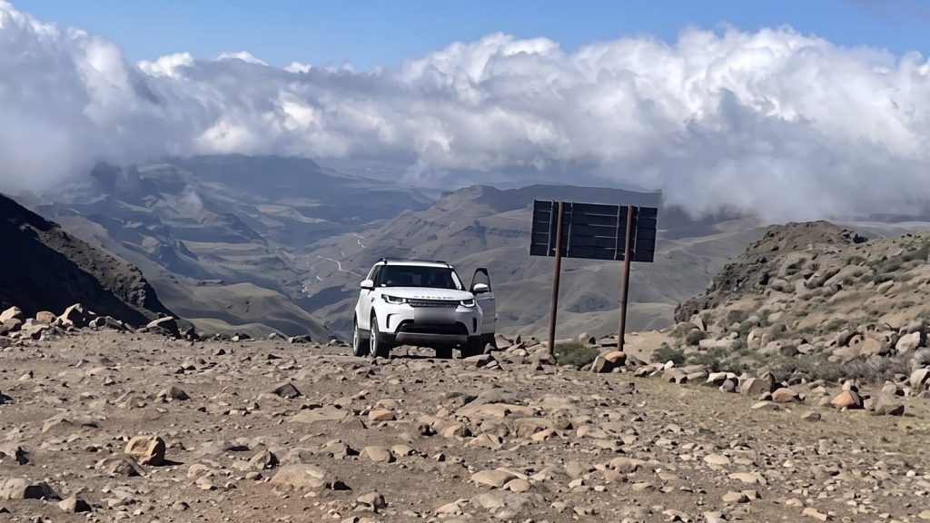 A luxury 4x4 on the rocky road at the top of Sani Pass with cloud in the valley below