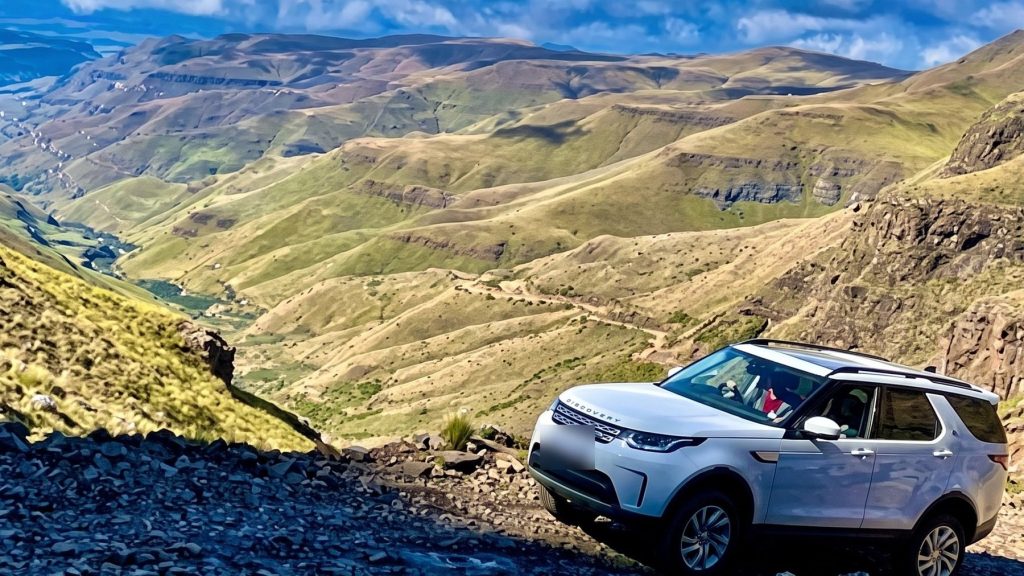 A luxury 4x4 parked on Sani Pass above a green folded valley